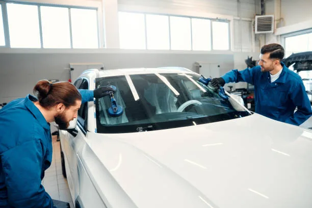 Auto glass technicians installing a new windshield on a vehicle in a repair shop